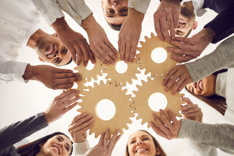 Group of people holding wooden cogs piecing them together
